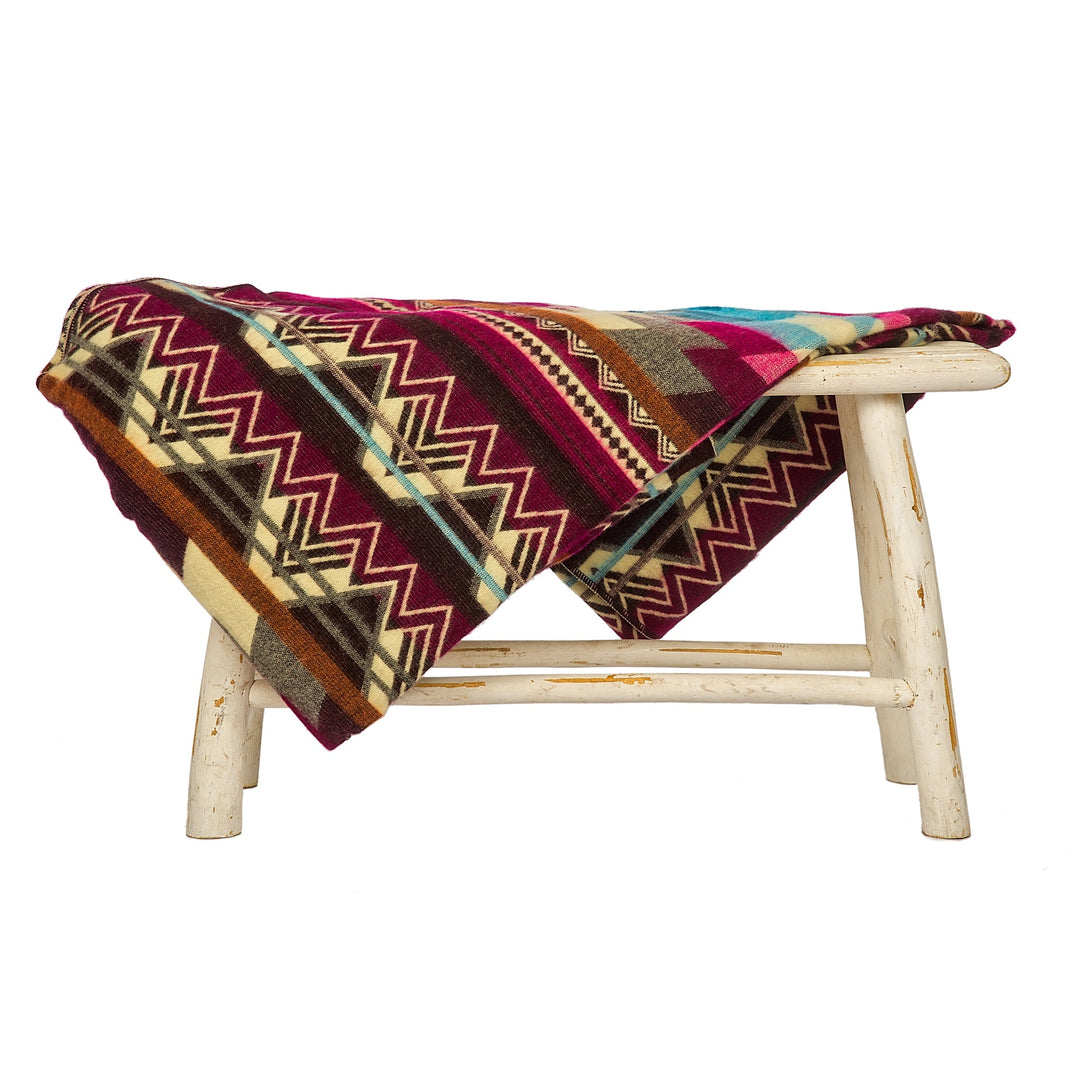 Wende-Alpaka-Decke, 'Antisana Lila', über einen rustikalen weißen Hocker drapiert, zeigt das dunkelgrüne Webmuster.