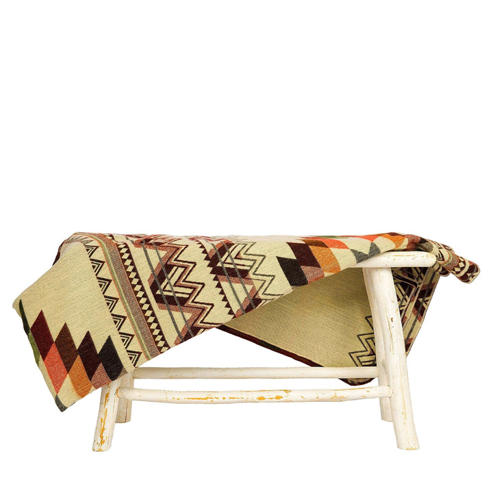 Wende-Alpaka-Decke, 'Antisana Orange', über einen rustikalen weißen Hocker drapiert, wobei die hellere beige Seite mit Zickzack-Mustern sichtbar ist.