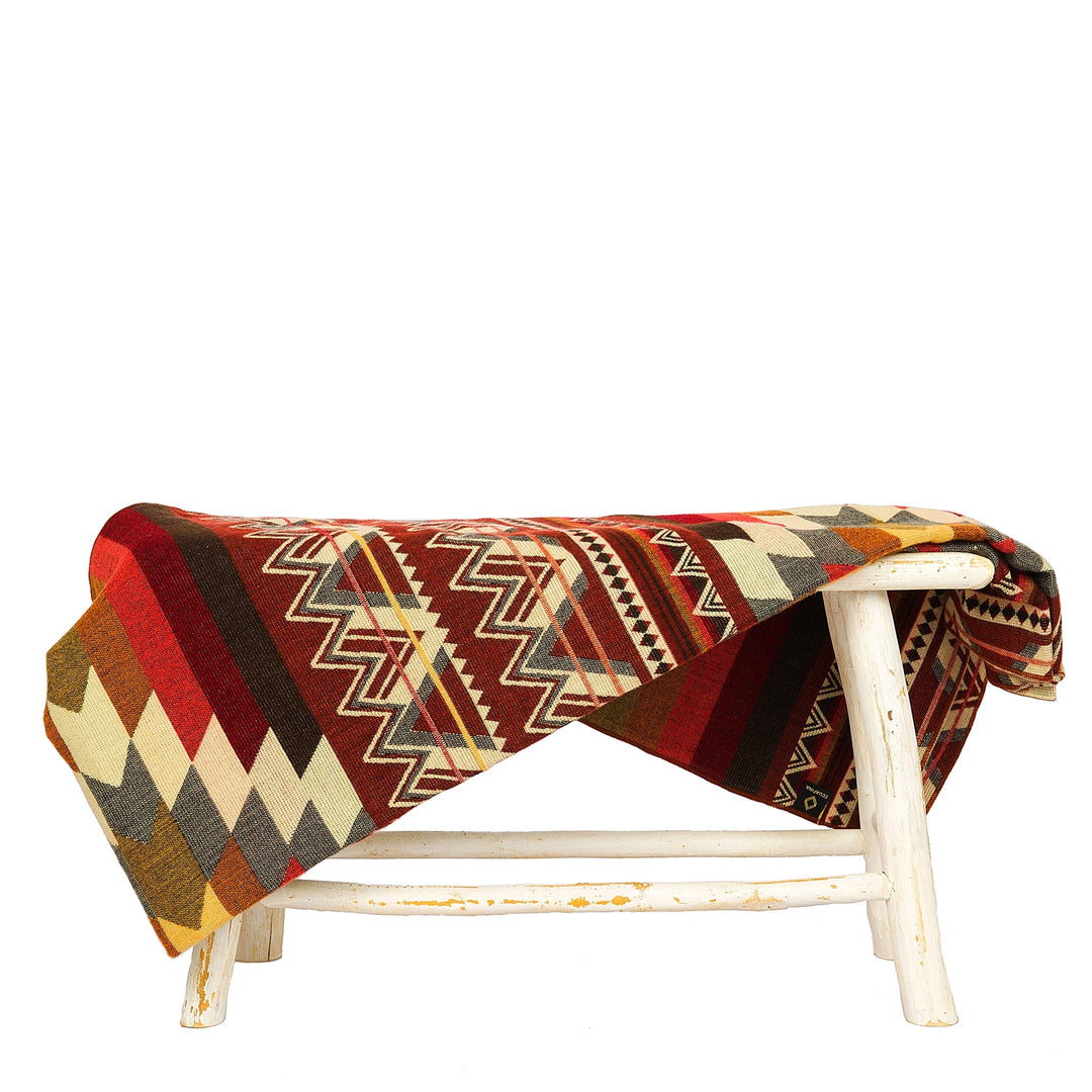 ewebte Alpaka-Decke, 'Antisana Orange', über einen weißen Hocker drapiert, die die reichen, mehrfarbigen geometrischen Muster präsentiert.