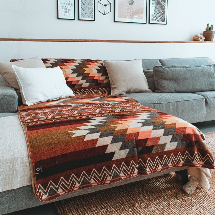 Alpaka-Decke, 'Antisana Orange', über ein modernes graues Sofa in einem Wohnzimmer drapiert, als farbenfroher, gemütlicher Akzent.