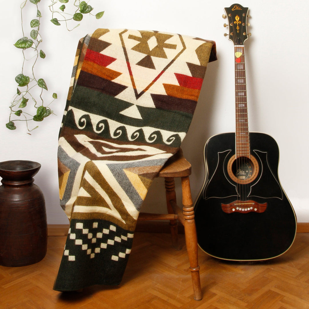 Alpaka-Decke 'Cayambe Grün' hängt über einem Holzstuhl neben einer schwarzen Gitarre als gemütliches Wohnaccessoire.