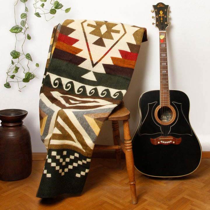 Alpaka-Decke 'Cayambe Grün' hängt über einem Holzstuhl neben einer schwarzen Gitarre als gemütliches Wohnaccessoire.