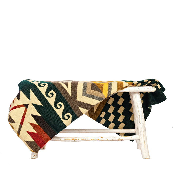 Wende-Alpaka-Decke, 'Cayambe Grün', über einen rustikalen weißen Hocker drapiert, zeigt das dunkelgrüne Webmuster.