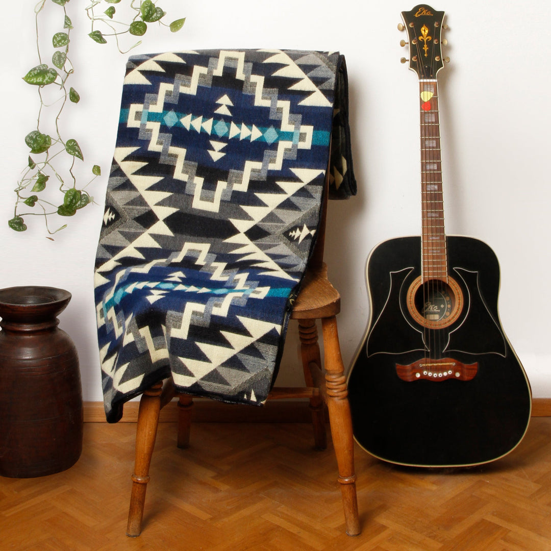 Alpaka-Decke 'Chimborazo Black' über einem Holzstuhl, akzentuiert eine schwarze Gitarre und Pflanzen in einem Raum.