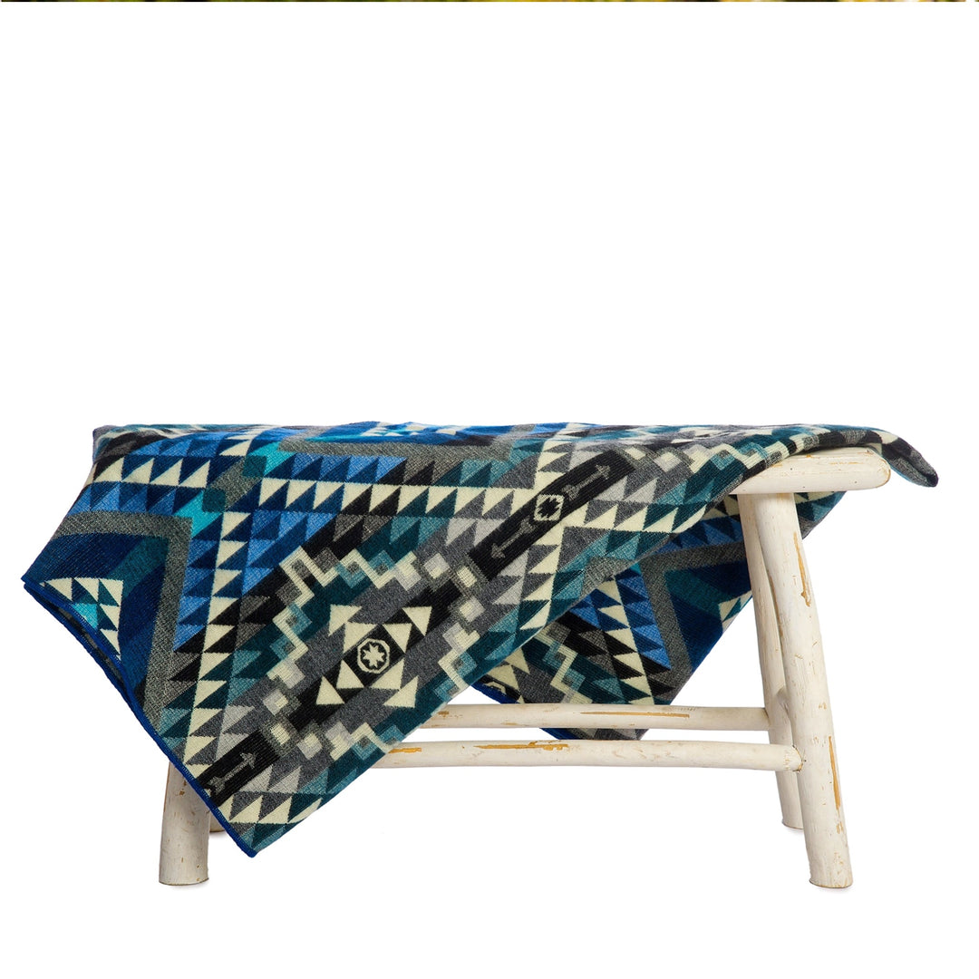 Alpaka-Decke 'Chimborazo Black' über einem weißen Hocker drapiert, präsentiert das dunkelblaue, graue Dreiecksmuster.