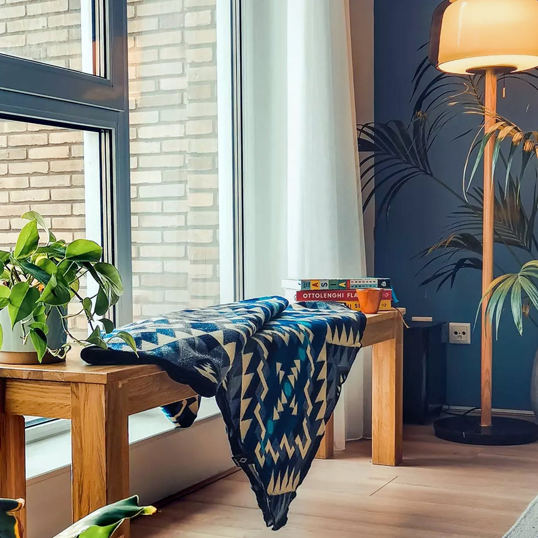 Alpaka-Decke 'Chimborazo Black' liegt auf einer Holzbank neben einem Fenster, dekoriert einen modernen Raum mit Pflanzen