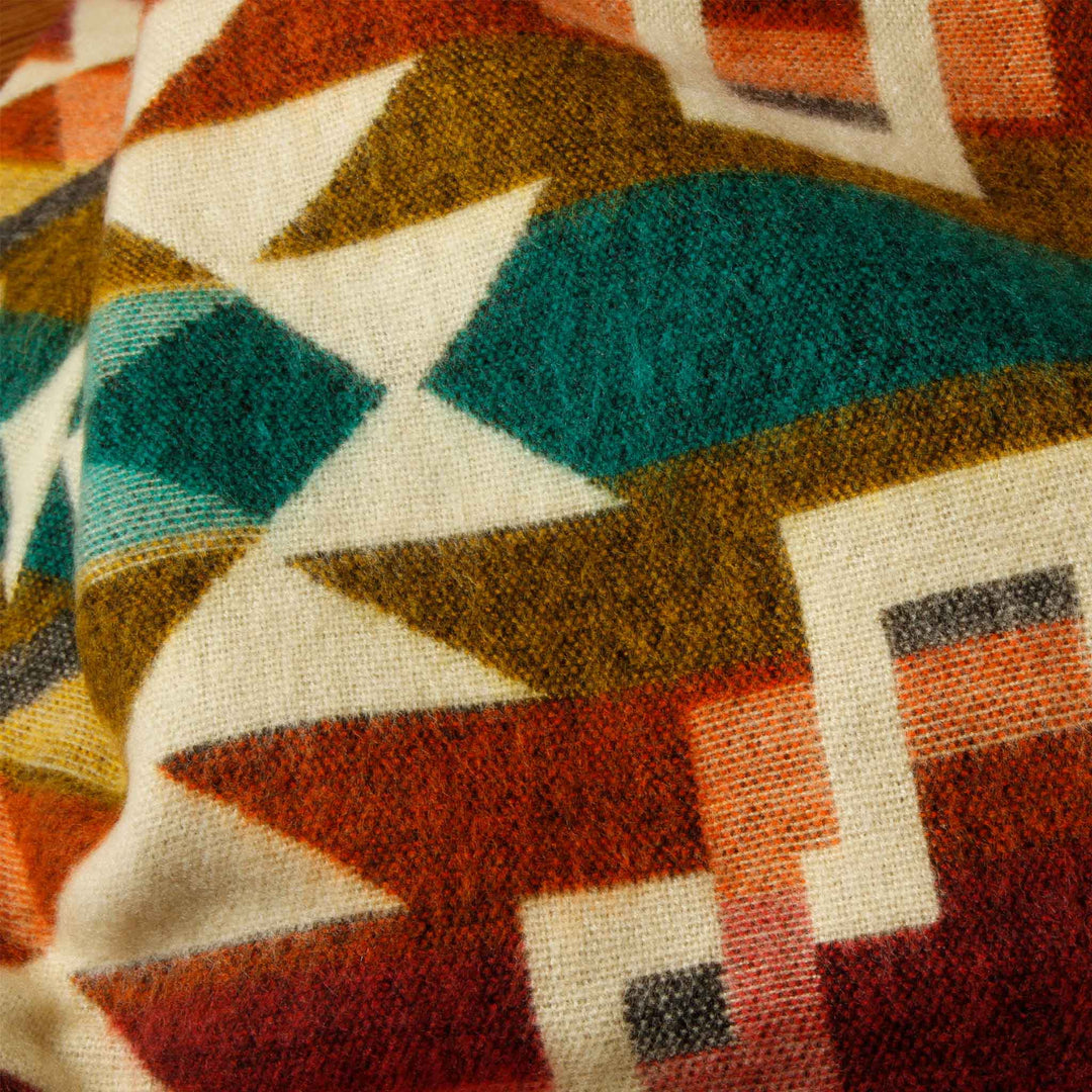 Struktur-Nahaufnahme der Alpaka-Decke 'Chimborazo Rosa' in warmen Farben und Türkis, die die Webarbeit zeigt.