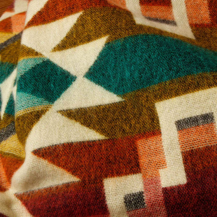 Struktur-Nahaufnahme der Alpaka-Decke 'Chimborazo Rosa' in warmen Farben und Türkis, die die Webarbeit zeigt.