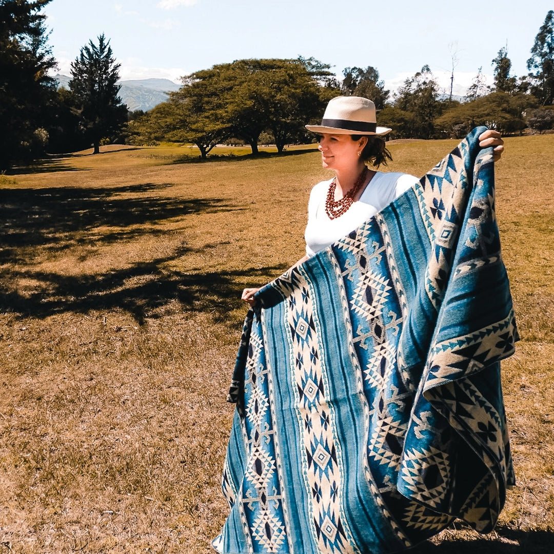 Frau mit Hut hält die blaue Alpaka-Decke 'Cotopaxi Blau' auf einer sonnigen Wiese in der Natur.