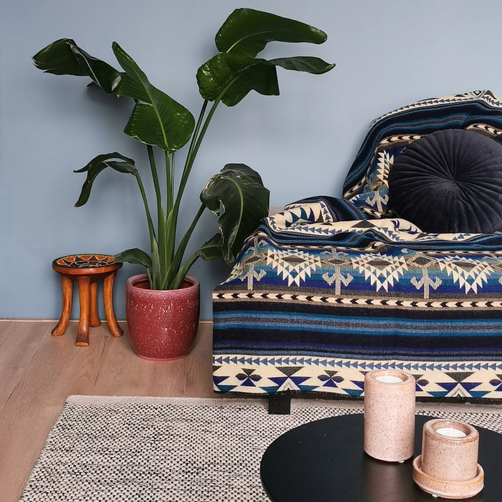 Alpaka-Decke 'Cotopaxi Blau' über eine Couch in einem modernen Wohnzimmer drapiert, mit großer Pflanze und dunkelblauem Akzent.