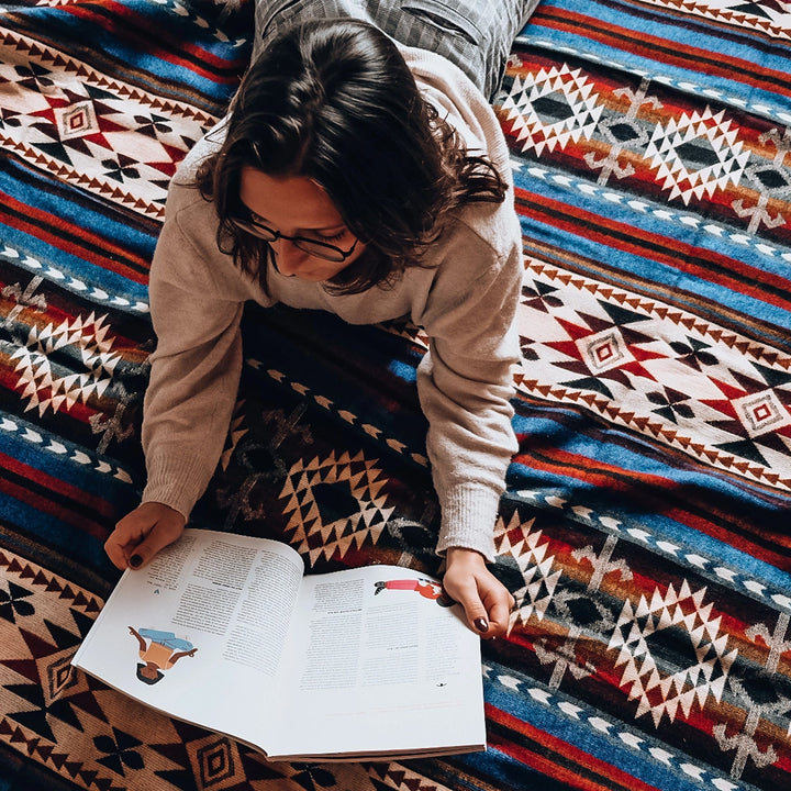 Alpaka-Decke 'Cotopaxi Blau' auf dem Boden ausgebreitet, mit Frau, die darauf einen Text schreibt