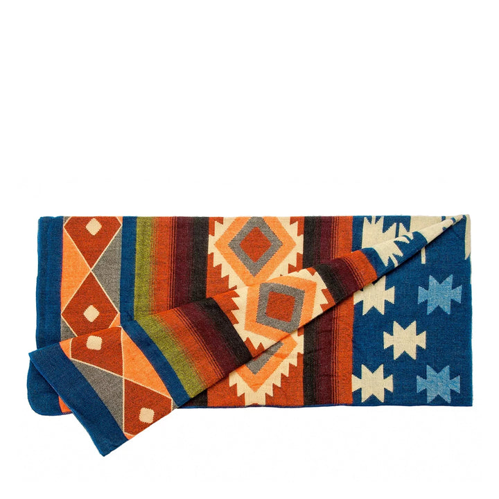 Die Alpaka-Decke mit dem bunten geometrischen Muster ist gefaltet dargestellt. Sie zeigt deutlich die verschiedenen Abschnitte mit Rauten in Orange und Streifen in Rot- und Erdtönen sowie einen blauen Abschnitt mit weißen Sternen