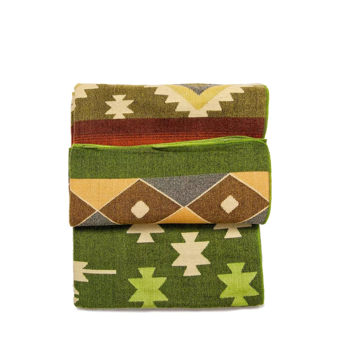 Die Alpaka-Decke mit dem bunten geometrischen Muster ist dreifach gefaltet und gestapelt dargestellt. Die verschiedenen Abschnitte in Grün, Orange, Braun und Gelb sind sichtbar