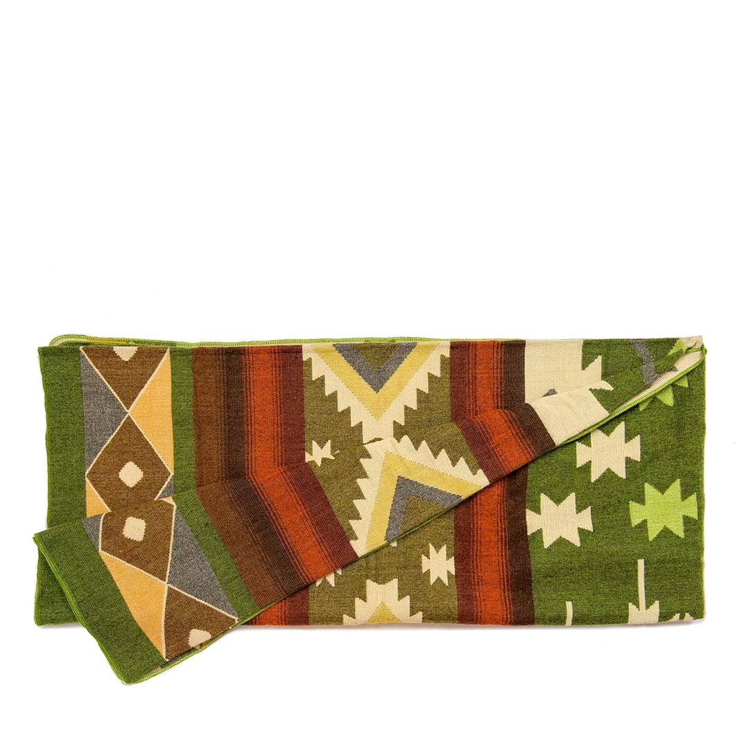 Die Alpaka-Decke mit dem bunten geometrischen Muster ist der Länge nach gefaltet. Sie zeigt Streifen- und Zickzack-Muster in Grün, Orange, Braun und Beige