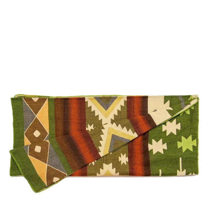 Die Alpaka-Decke mit dem bunten geometrischen Muster ist der Länge nach gefaltet. Sie zeigt Streifen- und Zickzack-Muster in Grün, Orange, Braun und Beige