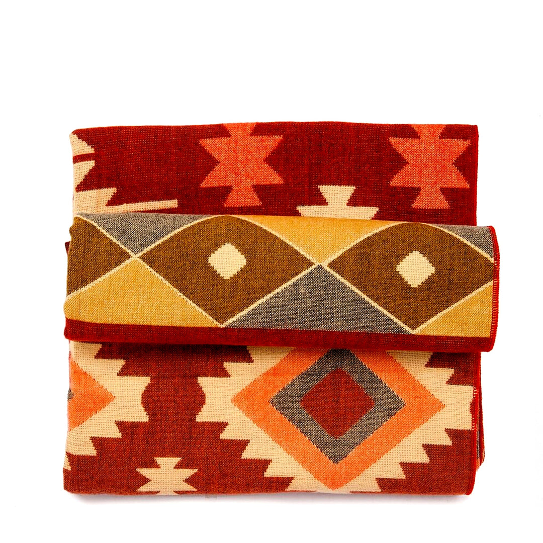 Die Alpaka-Decke mit dem bunten geometrischen Muster in Rot, Beige, Orange, Braun und Gelb ist dreifach gefaltet und gestapelt dargestellt, wobei verschiedene Musterabschnitte sichtbar sind. Der Hintergrund ist weiß