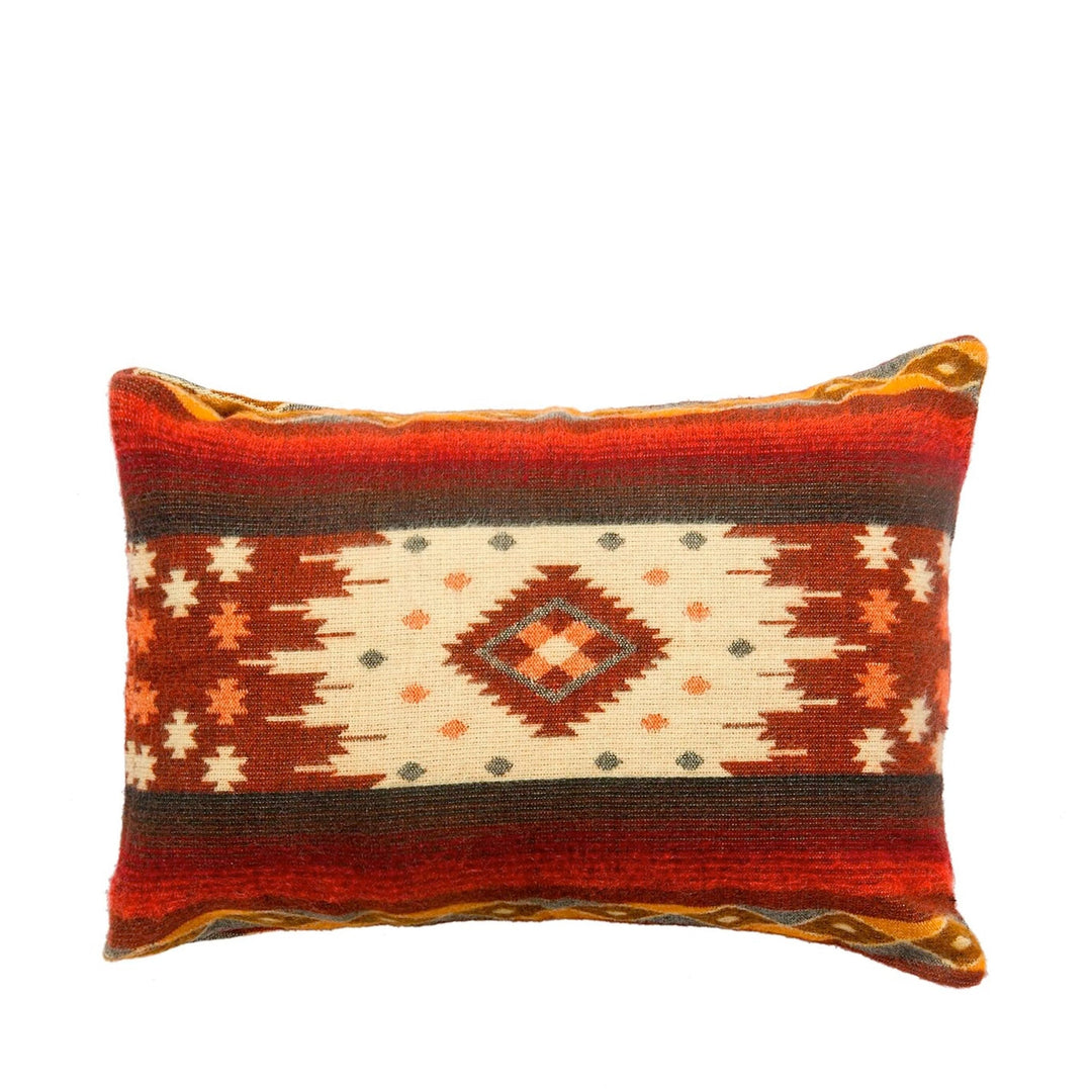 Rechteckiges Alpaka-Kissen mit einem traditionellen geometrischen Muster, dominiert von Rottönen, Orange, Beige und Dunkelbraun. Es zeigt ein zentrales Rautenmotiv auf hellem Grund, umgeben von sternförmigen Mustern und farbigen Streifen