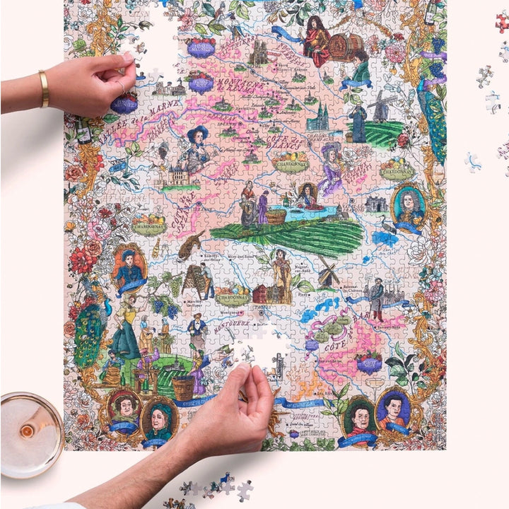 Gesamtansicht des fast fertigen 1000-Teile-Puzzles "The World of Champagne", wobei Hände die letzten Teile in die Karte der Weinregionen einfügen.