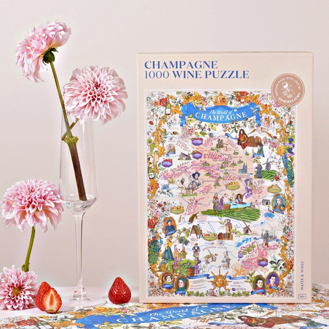 Produktaufnahme der Champagner-Puzzle-Box neben einem eleganten Sektglas mit drei rosa Dahlien und frischen Erdbeeren, vor einem hellen Hintergrund.