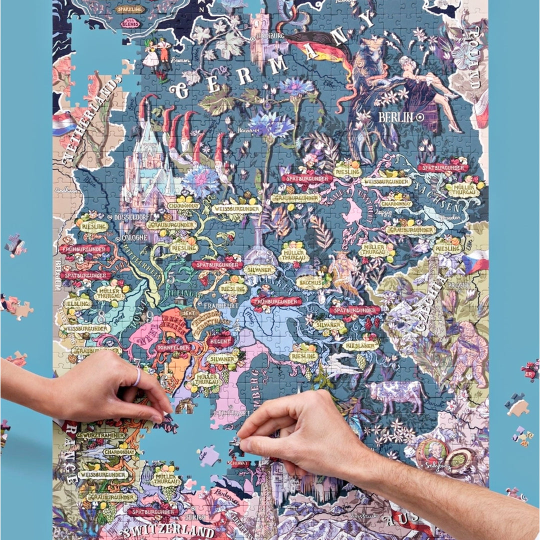 Zwei Hände setzen Puzzleteile in die illustrierte Landkarte der deutschen Weinregionen, mit Fokus auf die Mitte und den Süden Deutschlands.