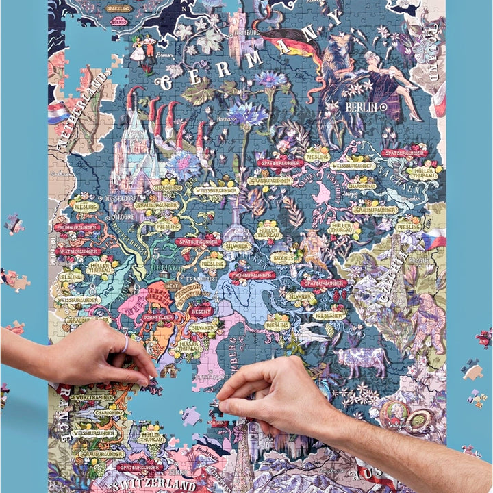 Zwei Hände setzen Puzzleteile in die illustrierte Landkarte der deutschen Weinregionen, mit Fokus auf die Mitte und den Süden Deutschlands.
