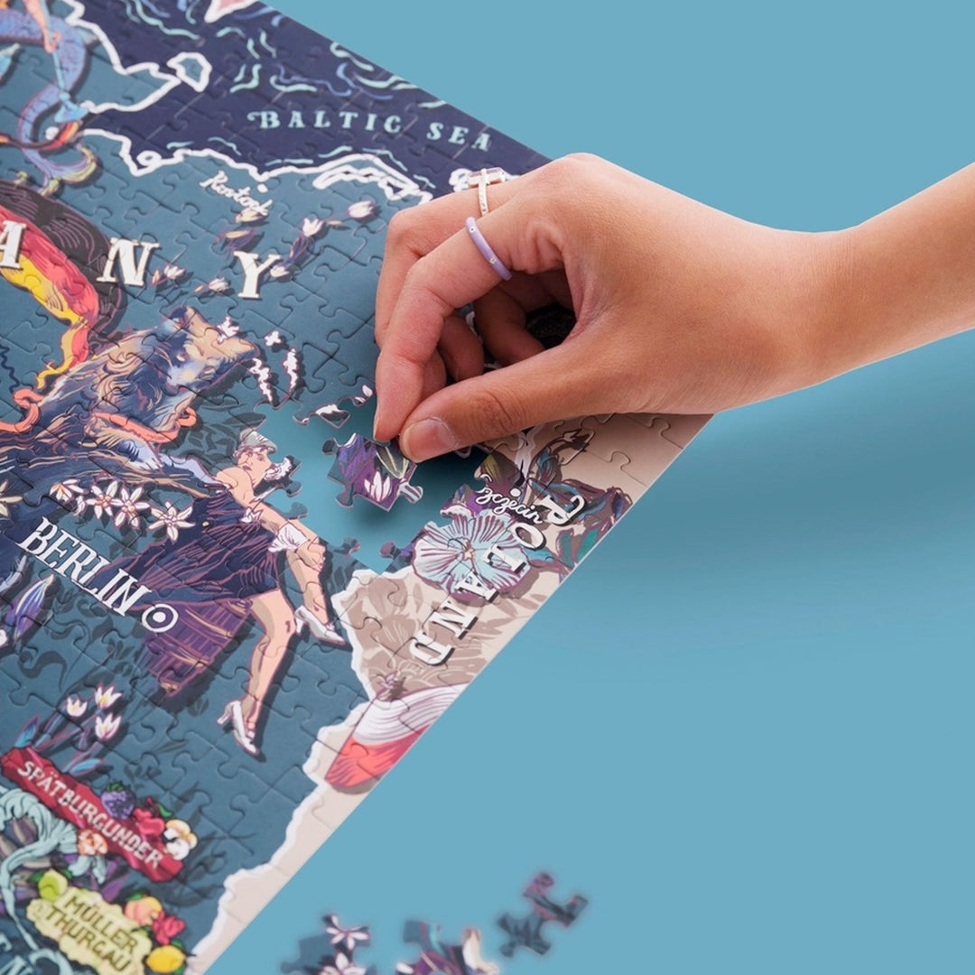 Hand setzt ein Puzzleteil in die Region um Berlin/Brandenburg des Deutschland-Puzzles ein. Die Karte zeigt die Ostsee und Spätburgunder.