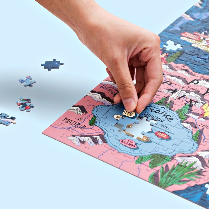 Zwei Hände fügen Puzzleteile in die illustrierte Landkarte Frankreichs ein, mit Fokus auf die Mitte (Loiretal, Bordeaux, Burgund).