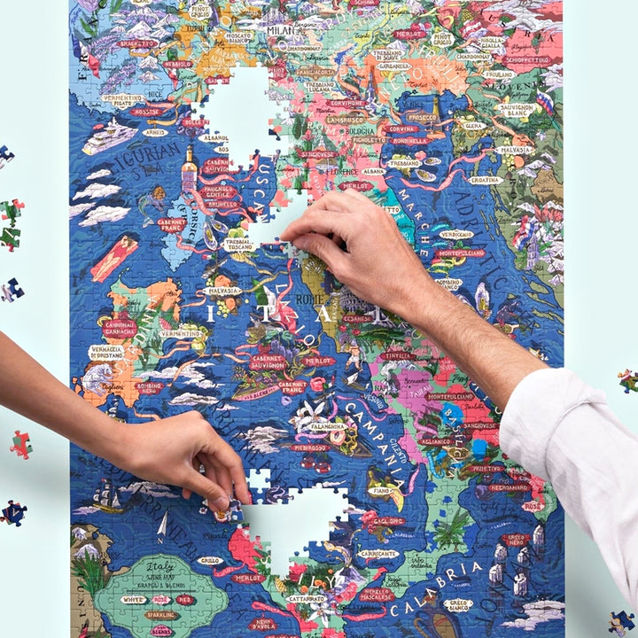 Zwei Hände fügen Puzzleteile in die illustrierte Landkarte Italiens ein, mit Fokus auf die Mitte (Toskana, Rom, Kampanien).