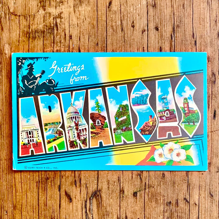 Vintage-Postkarte "Greetings from ARKANSAS" auf blau-gelbem Grund, der Schriftzug ist mit Sehenswürdigkeiten des Staates gefüllt und zeigt Baumwollblüten.