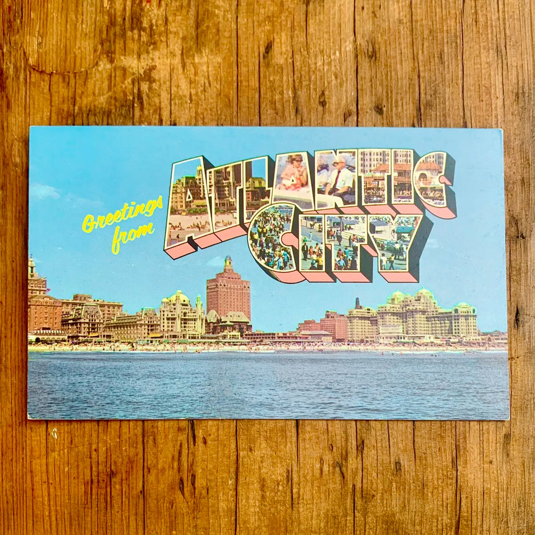 Vintage-Postkarte "Greetings from ATLANTIC CITY" mit einem breiten Blick auf die Küstenlinie, der Schriftzug zeigt Bilder von Menschenmengen und Attraktionen.