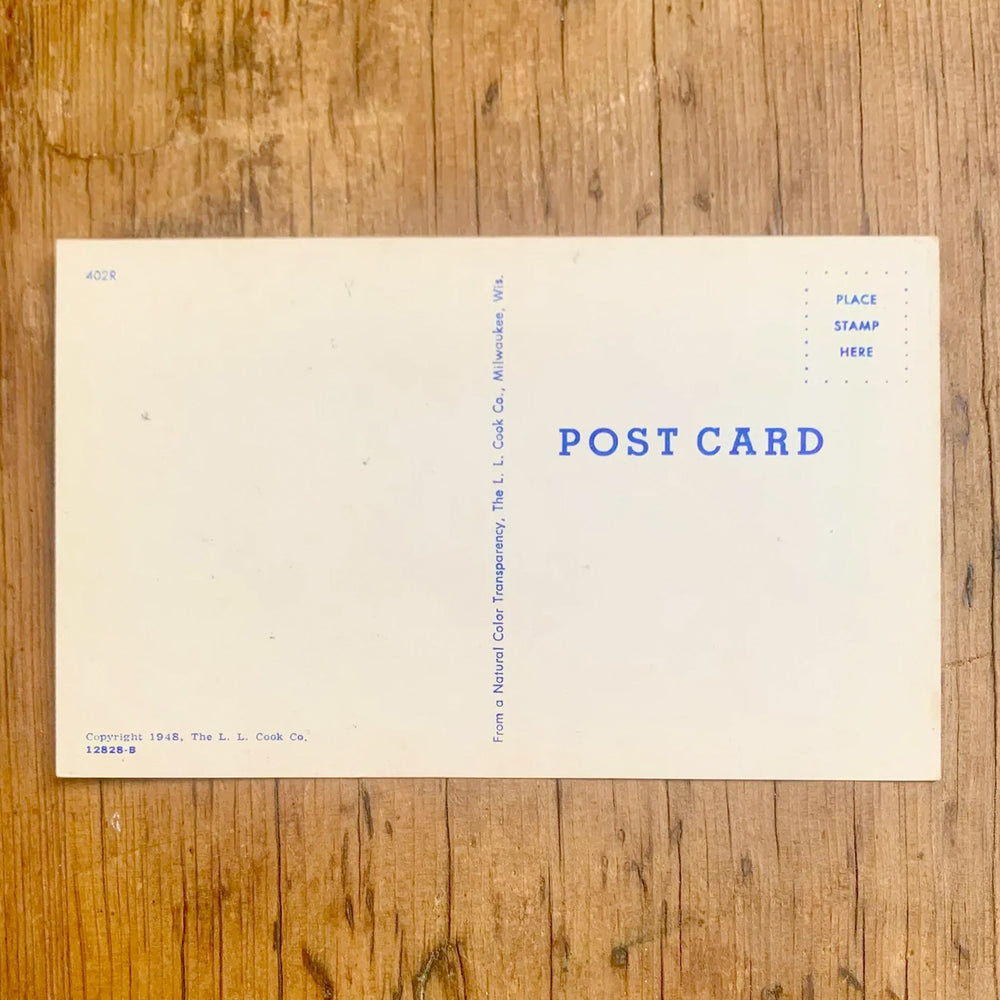 Rückseite von Dunkle Vintage-Postkarte "Greetings From Okoboji Lakes IOWA". Die Buchstaben zeigen Seemotive und das Ufer, mit stilisierten Zeichnungen von Menschen, die schwimmen und sich sonnen, im Vordergrund.