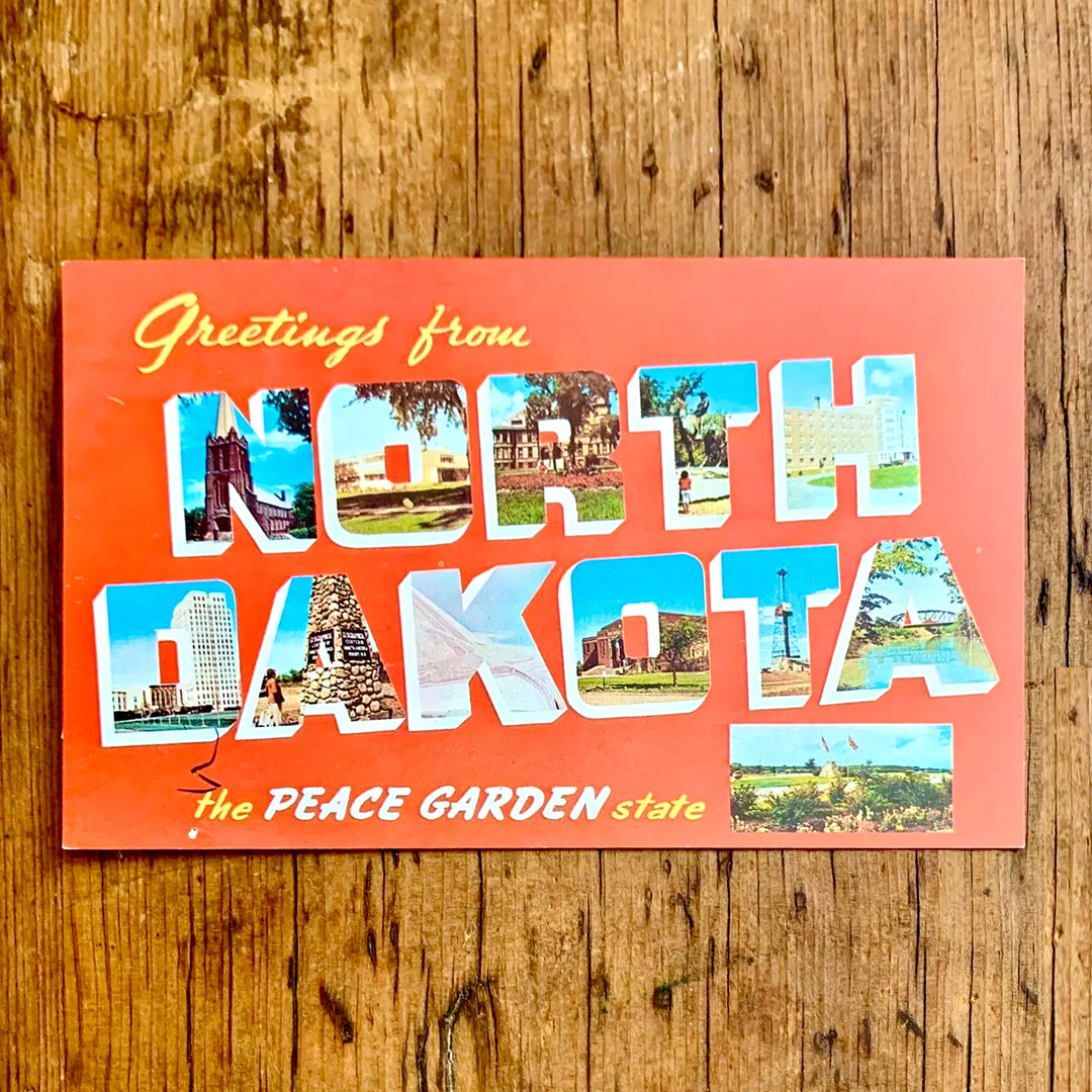 Vintage-Postkarte "Greetings from NORTH DAKOTA The PEACE GARDEN state" auf leuchtend rotem Hintergrund. Die Großbuchstaben zeigen Bilder von Wahrzeichen und Landschaften des Staates.