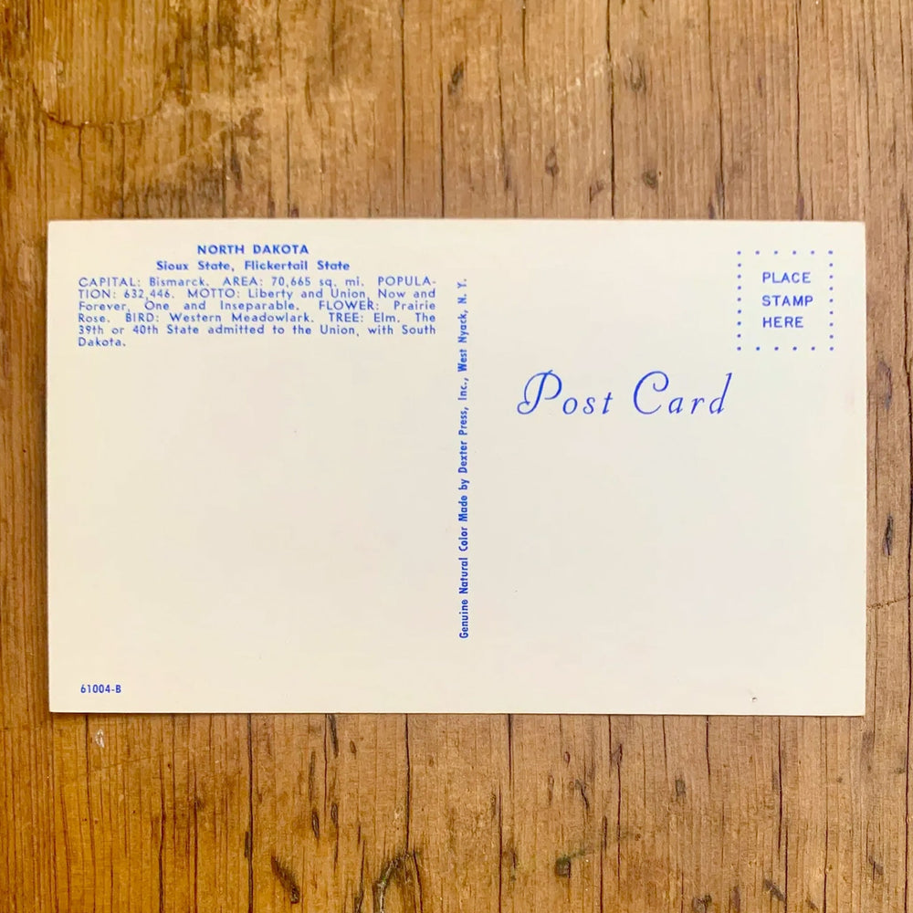 Rückseite von Vintage-Postkarte "Greetings from NORTH DAKOTA The PEACE GARDEN state" auf leuchtend rotem Hintergrund. Die Großbuchstaben zeigen Bilder von Wahrzeichen und Landschaften des Staates.